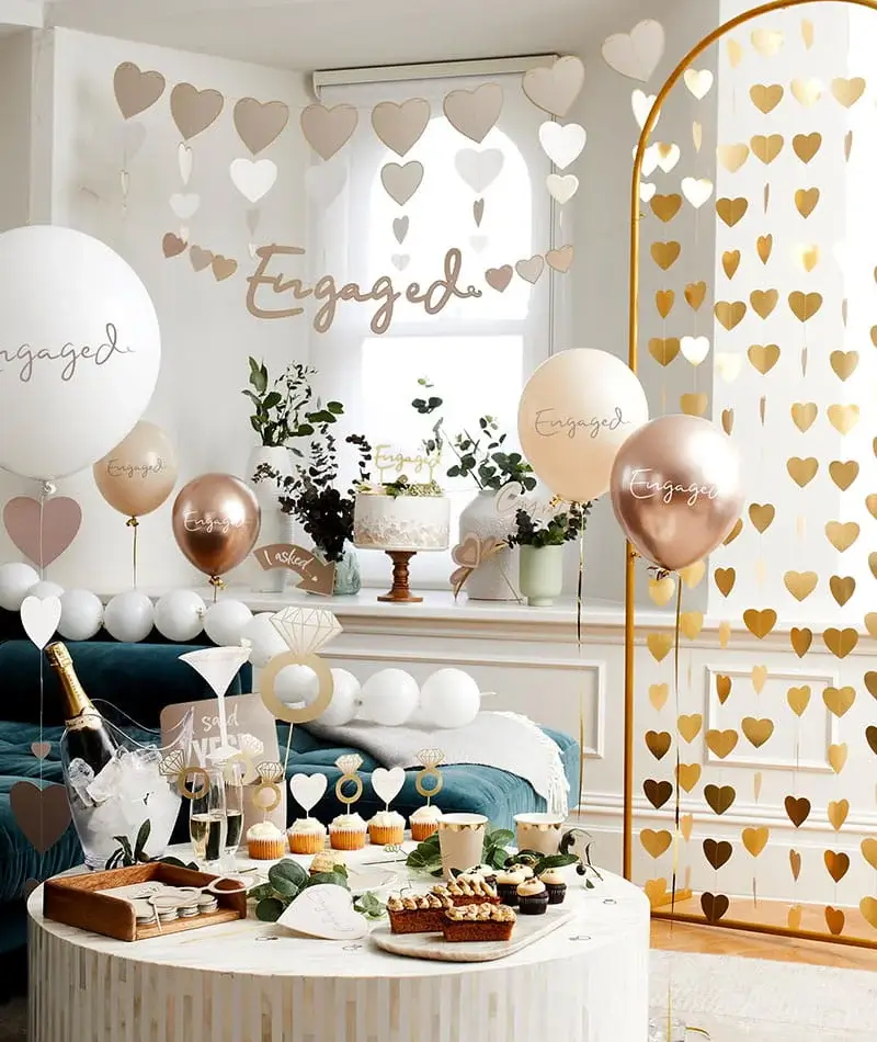 Engagement party setup with rose gold and cream balloons, heart decorations, a dessert table, and celebratory engagement-themed décor. Engagement party setup with rose gold and cream balloons, heart decorations, a dessert table, and celebratory engagement-themed décor.
